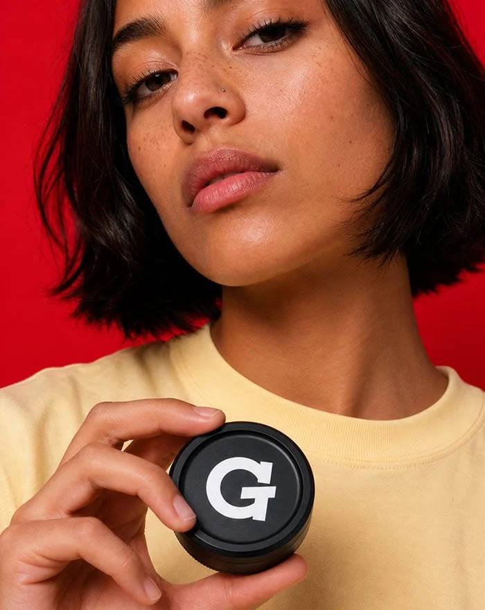 Woman holding up the black G Pen 3-Piece Slim Grinder on a red background